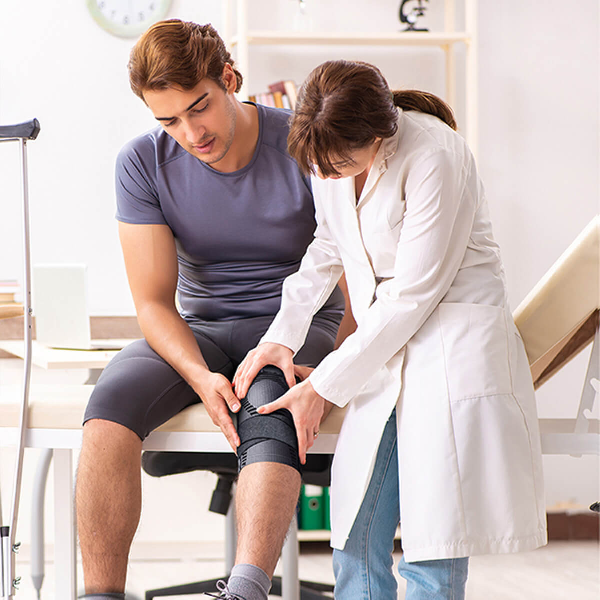 A healthcare professional assists a patient with knee support in a clinical setting.